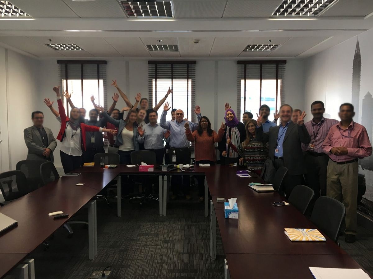 A large multicultural team standing together with raised hands in a meeting room