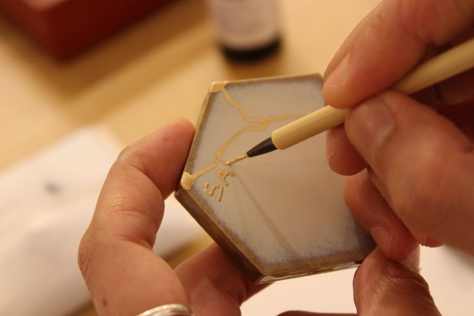 Hands applying gold to a ceramic piece during Kintsugi practice